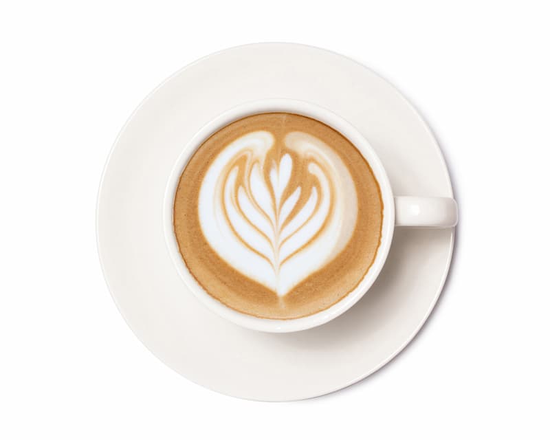 a cup of milk with a heart design on the foam, served on a white saucer on a white background.