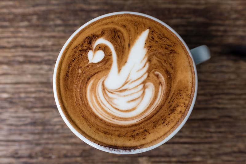 a cup of coffee with latte art in the shape of a swan, top view, on a wooden surface.