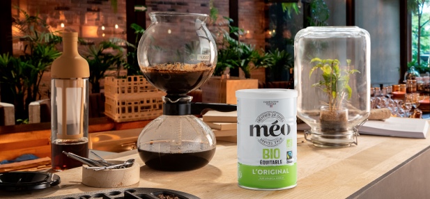 Countertop coffee maker with siphon coffee maker and Meo organic coffee container. in the background there is a glass vase with a plant.