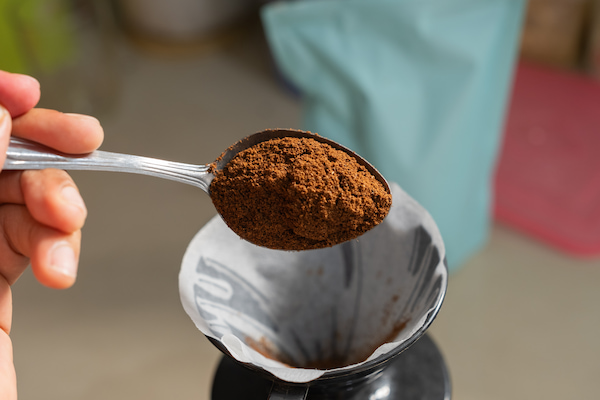 hand holding a spoon of ground coffee on a paper filter in a coffee maker.