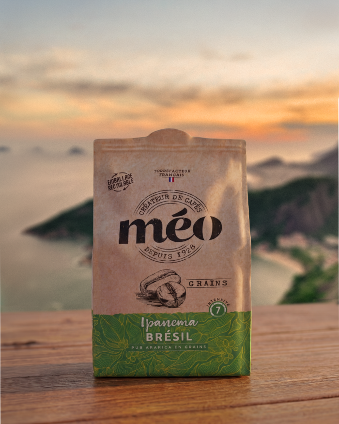 a bag of méo ipanema brazil coffee beans is placed on a wooden surface, with a blurry outdoor landscape and sunset in the background.