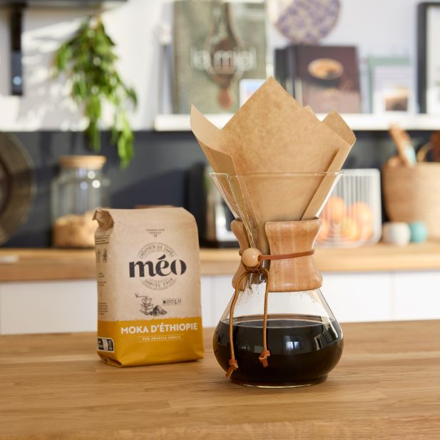 a chemex coffee pot with brewed coffee sits next to a bag of ethiopian mocha coffee beans on a wooden counter in a kitchen.