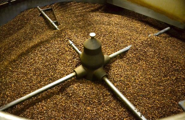 a large cylindrical machine filled with roasted coffee beans, equipped with rotating metal arms to evenly distribute and cool the beans.