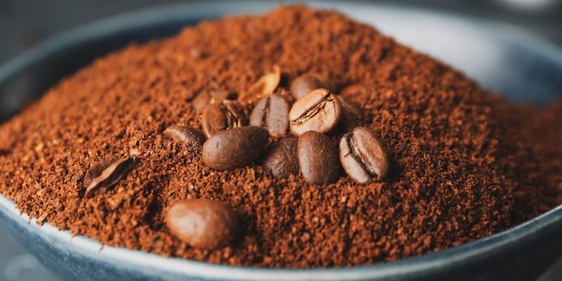 closeup of whole coffee beans resting on a pile of ground coffee in a dark bowl.