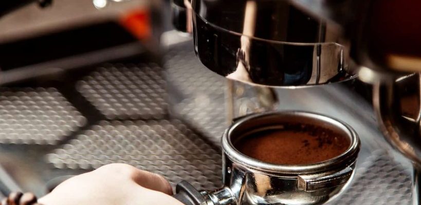 a hand holding a filter holder inserted into an espresso machine.