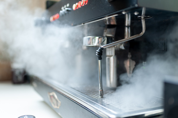 close-up of a coffee machine with steam coming out of the steam nozzle, indicating its operation.