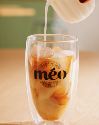 a hand pours milk into a glass of cold coffee with the logo printed on it "distortion".