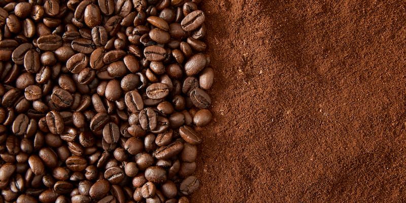 coffee beans on the left and ground coffee on the right, next to each other on a flat surface.