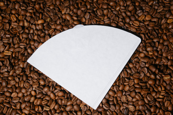 a white paper coffee filter rests on a bed of roasted coffee beans.