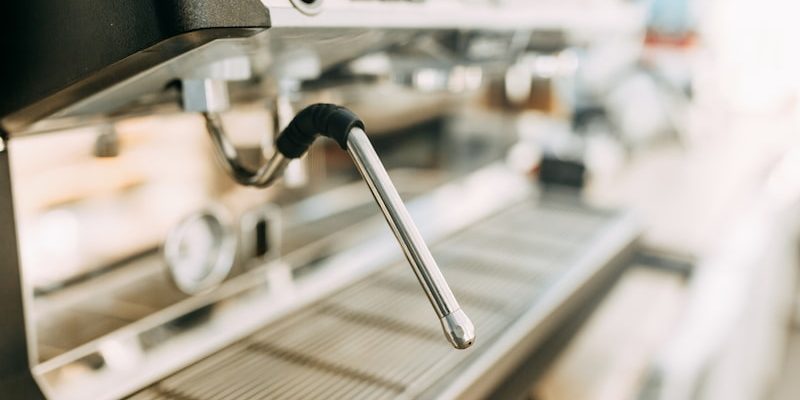 close-up view of a metal steam wand on a coffee machine, positioned above the drip tray.