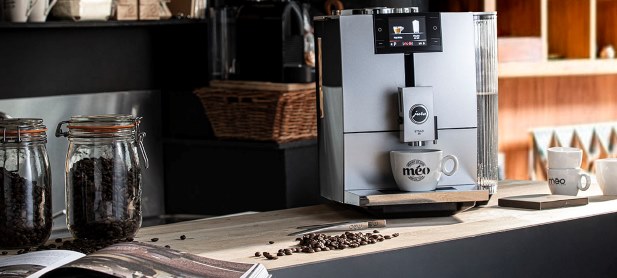 a modern espresso machine on the kitchen counter with a cup of coffee under the dispenser. nearby there are two pots of coffee beans.