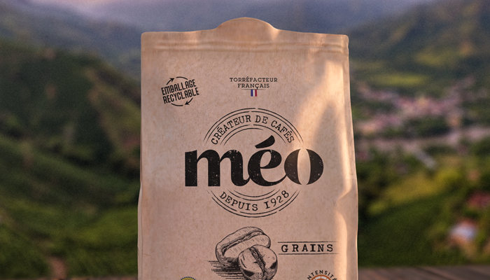 a bag of méo timaná colombia coffee beans sits on a surface with a blurry mountain landscape in the background.