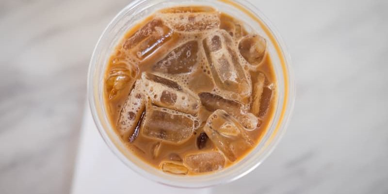 top view of an iced coffee in a clear plastic cup, filled with ice cubes, placed on a white napkin on a light marble surface.