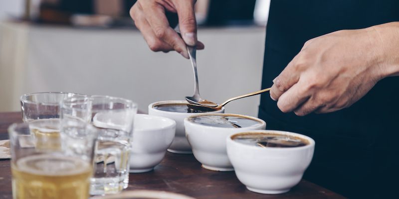 person carrying out a coffee tasting with several bowls and glasses on a table.